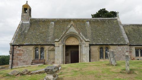 An old church building with gravestones - some toppled over - in front of it