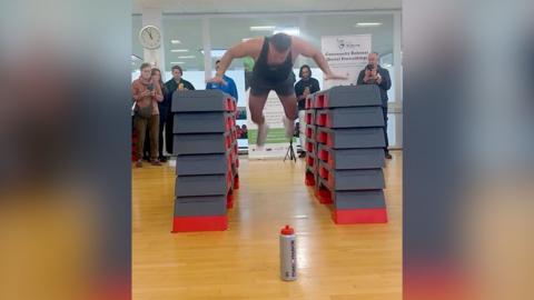 A man in gym clothes pictured mid-air between two towers of foam blocks about a metre high.