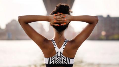 Rear view of female jogger with hands behind head, wearing black and white geometric sports bra.