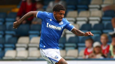 Kadeem Harris running on the pitch with his arms out to his sides during a pre-season game for Gillingham. He is wearing a blue Gillingham shirt with white shorts