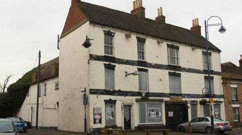 The three-storey building as it was in 2012. The door and windows have been boarded up and the cream paint on the bricks has been chipped. 