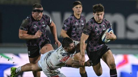 Sam Worsley (right) of Bristol Bears runs with the ball under his arm as he is almost tackled by a Scarlets player