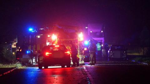 A night-time shot showing a car on a road, a fire engine and members of the emergency services in the background 