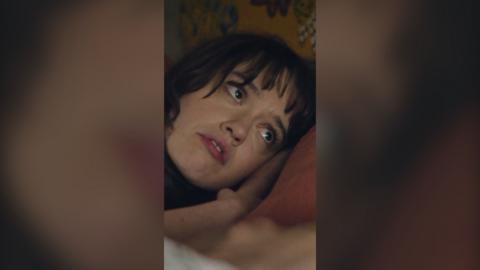 Aimee Lou Wood lying down in bed with her head on the pillow looking at her sleeping partner