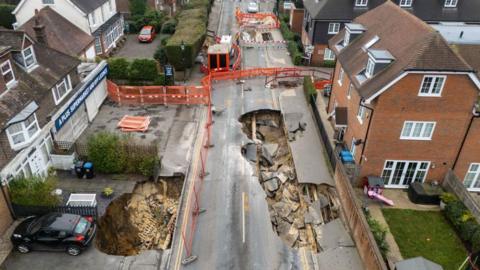 An aerial image of a sinkhole in a road, with houses to the left and right