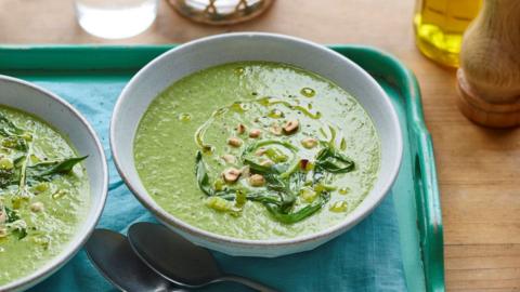 White bowl filled with green soup topped with a sprinkling of nuts and leafy greens