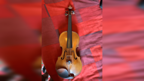 The brown, wooden violin lying on a patterned red fabric. 