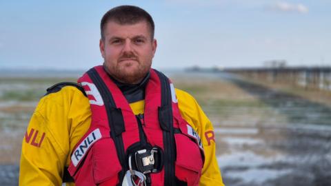 A man wearing a life jacket and standing in front of Southend Pier