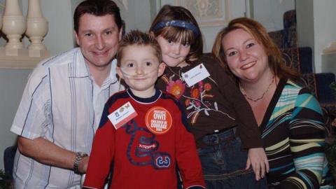 A family of a man, woman and two children, a young girl and boy. The boy is wearing a red top and has a tube which goes into his nose. Chris, Matthew, Laura and Lisa Hayden-Johnson