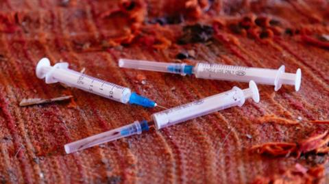 Three syringes, seemingly used, lying on a tattered orange blanket