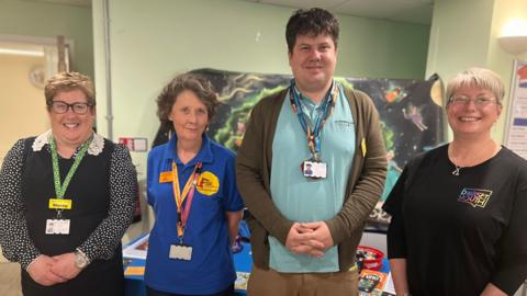 A photo of four people standing in a row looking at the camera. 