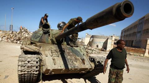 A picture taken on November 9, 2017 shows members of the self-styled Libyan National Army, loyal to the country's east strongman Khalifa Haftar, riding on a tank as it drives down a street through the rubble in Benghazi's central Akhribish district following clashes with militants