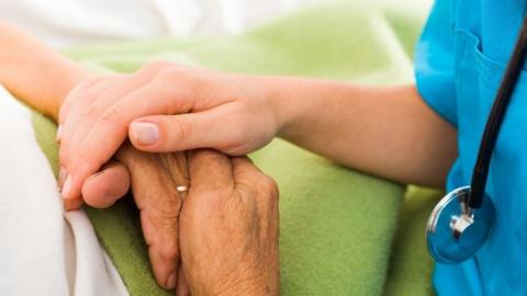 Social care provider holding senior hands in caring attitude - helping elderly people