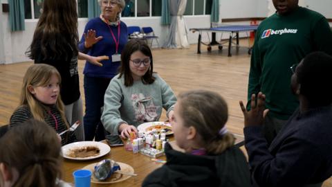 A group of young carers sit around a table with pancakes chatting