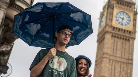 Man holding an umbrella near Big Ben with a woman.