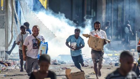 People run with merchandise as crowds leave shops with looted goods amid a state of unrest in Port Moresby on January 10, 2024