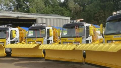 A row of yellow gritting vehicles at a depot.