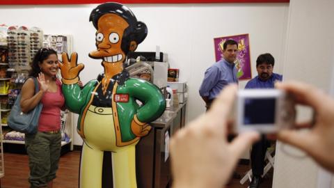 A woman poses for a photograph alongside cartoon statue of character of Apu