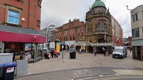 A street view of Blackpool town centre with the Grand Theatre in the centre and rows of shops going off to each side of the street. 