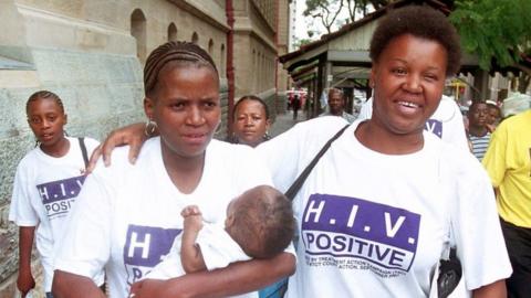 Two women wearing HIV Positive t-shirts smile at the camera