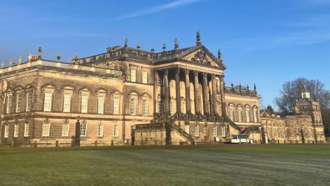 A stately home with huge pillars around the entrance and large lawns at the front.