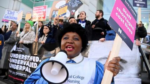 A nurse with a megaphone stands in front of the picket line outside University College Hospital in London