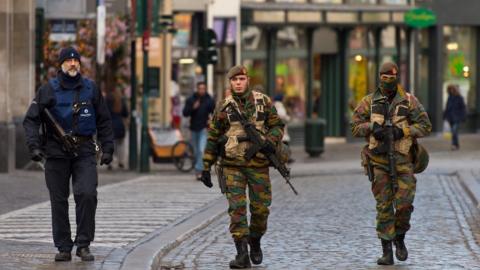 An armed policeman and two soldiers guard the shops on Rue Du Marche Aux Herbes on 23 November 2015 in Brussels