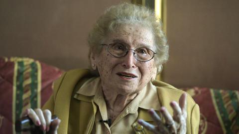 Rosa Roisinblit smiles and gestures at the camera during an interview with AFP in Buenos Aires, 2016. She wears a pale mustard jacket and matching shirt, holding a walking cane in her right hand. Her nails are painted pink, and she wears wire-rimmed spectacles. 