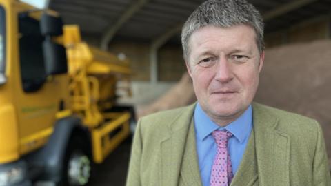Richard Clewer - in a suit and tie - looks into the camera from a council depot