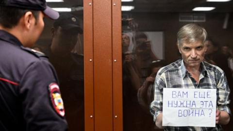 Moscow city deputy Alexei Gorinov, stands with a poster reading ""Do you still need this war?" i