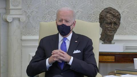 President Biden sitting down and wearing a black face mask.