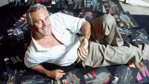 Giorgio Armani lying on dozens of black sheets showing clothes sketches on the floor, in 1982