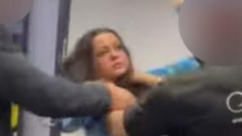 A screenshot of the viral video shows Amarii, wearing a two-piece outfit with a pattern of light and dark blue shades. She's facing a bouncer, who appears to have his hands around her neck. She appears distressed. A second man is just outside the shot, but his arm is close to Amarii and the other man.