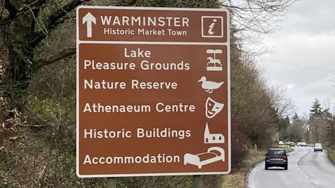 A brown tourism road sign for Warminster