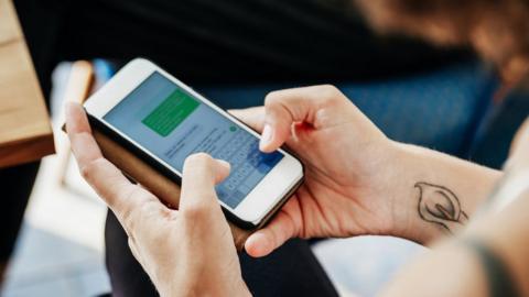 Person texting someone on an iPhone with green-coloured messages displayed on phone screen