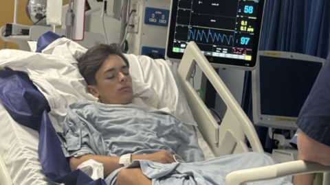 A teenager in a hospital bed attached to a monitor with his eyes closed