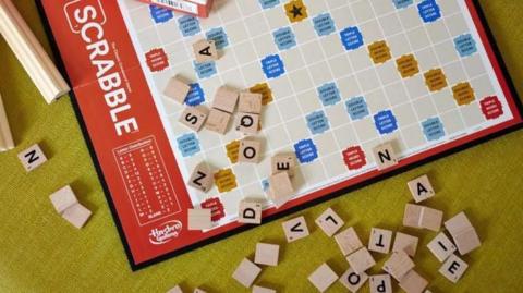 A Hasbro Scrabble board game arranged on a table alongside the box, tiles, and racks.