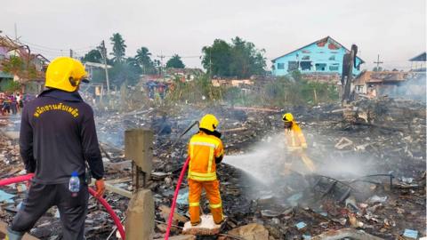 Thai firefighters extinguishing a fire after an explosion at a firework warehouse