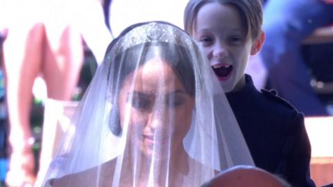 The son of Ben Mulroney smiles as he holds Meghan Markle's dress on 19 May