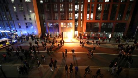 A bin set on fire surrounded by a large crowd