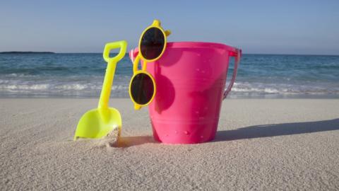 A bucket, spade and sunglasses on a beach