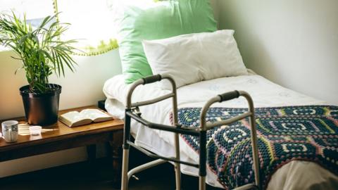 The inside of a care home room with a walking frame and bed