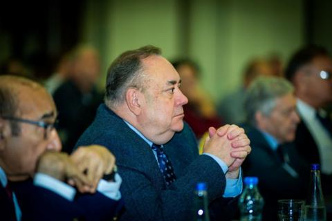 Alex Salmond looking at conference stage with elbows resting on table