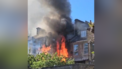 Flames and smoke can be seen pouring out of a tall London-style town house 