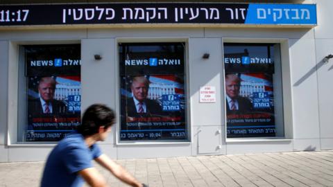 A man cycles past images of Donald Trump displayed on monitors in Tel Aviv, Israel (9 November 2016)