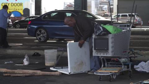 An unhoused man collects his possessions