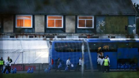 People are seen collecting belongings before boarding a bus inside an immigration processing centre in Manston