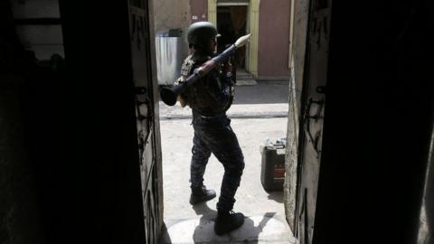 a man in combat gear standing in a doorway holding a weapon