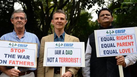 Pascal Mazurier (C), an ex-French consular officer who once worked for the French Consulate in Bangalore, holds a placard along with his father Jack Mazurier (L) after a press conference in Bangalore on June 17, 2015.