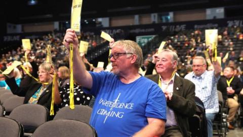Man holds up his accreditation at the SNP conference